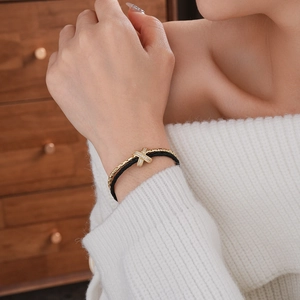 Detail of gold and black braided double-layer bracelet with crisscross zircon charm