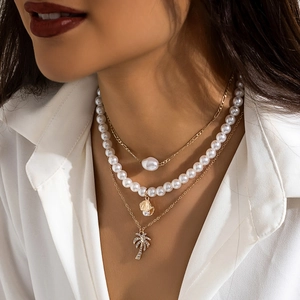 Detail of layered gold necklace with white pearls, seashell and rhinestone palm tree charm