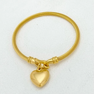 Macro detail of golden twisted cable bracelet featuring a polished heart pendant charm