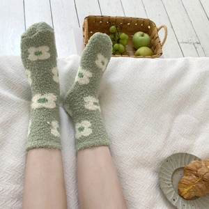 Detail of green fuzzy socks with white floral patterns on a cozy white bed background