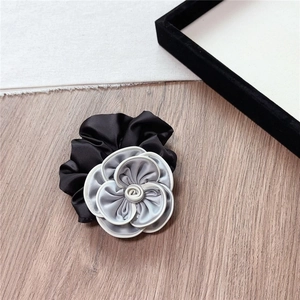 Detail of elegant satin camellia hair scrunchie with white edged petals on a wood surface