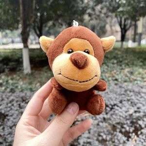 Cute brown monkey plush keychain accessory held against a natural outdoor background