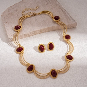 Parure de bijoux rétro dorés avec pierres ovales rouge foncé sur un fond de pierre