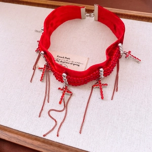 Gros plan d'un choker en velours rouge avec perles, pendentifs croix et détails de pompons