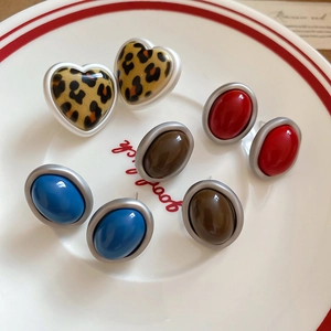 Detail view of acrylic leopard heart and oval stud earrings in a white ceramic dish