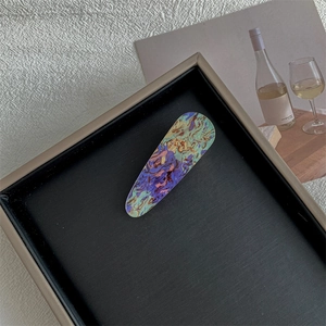 Detailed close-up of a long oval hair clip with colorful vintage marble textures on a tray