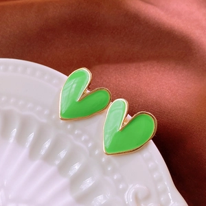Detailed macro view of heart-shaped green enamel stud earrings on a ceramic dish