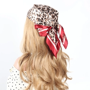 Leopard print satin head scarf with red border worn on wavy hair against white background