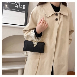 Detail of black evening clutch bag with golden leaf clasp held by a model in a trench coat