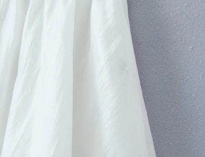 Detailed close-up of white silk-like fabric featuring delicate vertical pleats and lace trim