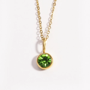Macro detail of a golden necklace featuring a polished round green gemstone pendant