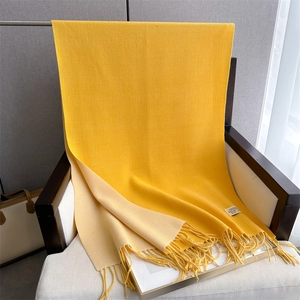 Detail of yellow and beige double-sided cashmere scarf with tassels on wooden chair