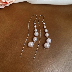 Detail shot of long pearl tassel earrings on a brown wood background with floral accents
