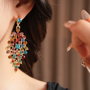 Detail of vintage gold-plated leaf earrings with colorful rhinestones on a model
