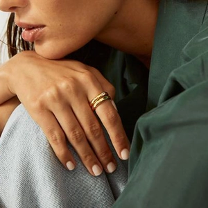 Set of two gold dome rings featuring clear and green zircon stones on model's hand