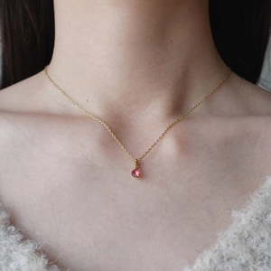 Dettaglio della collana dorata con piccolo ciondolo in zircone rosa indossata da modella