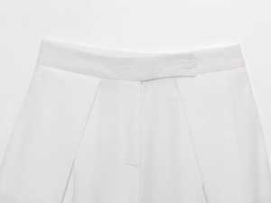 Detailed macro view of white woven fabric texture on high-waist pleated trousers