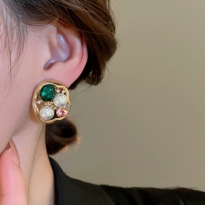 Close-up of vintage gold earrings with green gems and pearls on a model's ear