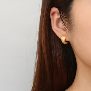 Close-up of a model wearing a gold geometric C-shaped earring with irregular hammered texture