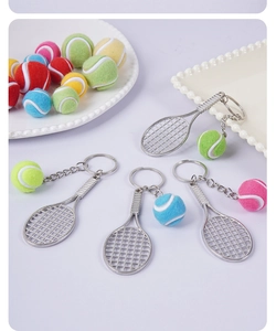 Detailed close-up of mini tennis racket and colorful felt ball keychains on white tray