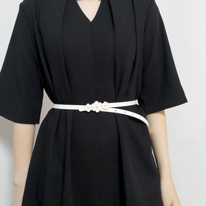 Macro shot of a thin white faux leather belt with a 3D floral buckle on a black dress