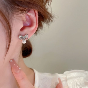 Close-up of elegant silver bow earrings with sparkling crystals and white round pearls