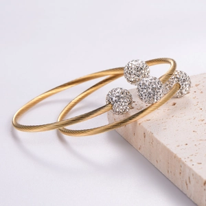 Gold stainless steel wire cable bangle set with rhinestone spheres on a stone pedestal