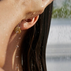Close-up of golden shell earring on wet skin showing waterproof 18k gold plating