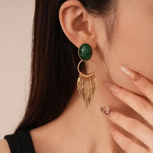 Detail shot of vintage green resin oval earrings with gold metal tassels worn by a model
