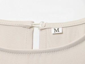 Macro detail of beige blouse neckline showing fine twill fabric texture and size M label