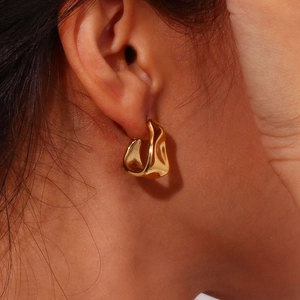 Irregular golden geometric earrings with textured metallic finish on model side view