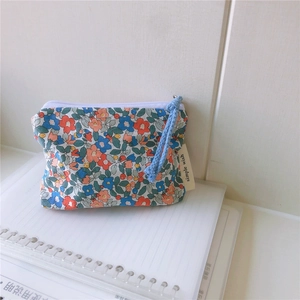 Close-up of small floral cotton pouch with blue zipper pull on a white notebook