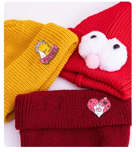 Detailed view of colorful knitted beanie hats with cat paw badge and plush eye decor