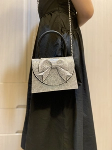 Silver rhinestone evening bag with bow detail and chain strap worn over black dress