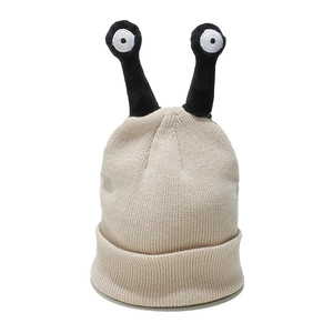Close-up of knit beanie featuring funny alien antennae and cartoon eyes on beige fabric