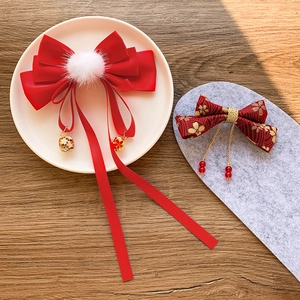 Detail of red bow hair clip with white fur ball and golden bell on a white tray