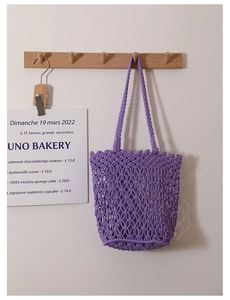 Detail of purple cotton mesh woven tote bag hanging on a wooden hook in a rustic setting