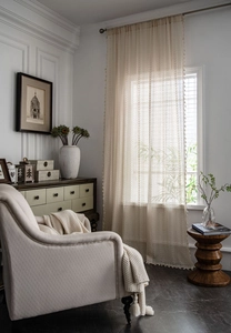 Close-up of beige crochet lace curtain with hollow knit patterns and elegant fringe trim