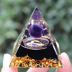 Close-up of crystal resin pyramid with amethyst ball, Aries symbol and gold leaf