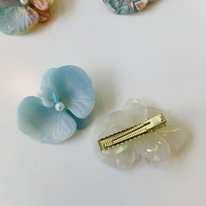 Close-up of floral acetate hair clip with pearl center and golden duckbill metal base