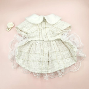 Detail of white tweed pet dress featuring gold threads, pearl buttons, and lace hem