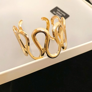 Detailed view of wide gold wave hollow-out open bangle with mirror polished metal surface