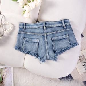 Dettaglio degli shorts in denim azzurro con bordi sfilacciati e tasche posteriori su fondo bianco
