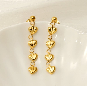 Détail de boucles d'oreilles longues à pampilles en cœur doré sur plateau blanc