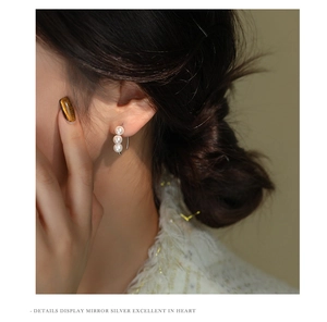 Detail view of triple white pearls vertically arranged on a silver hook earring