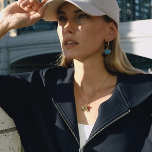 Close-up of golden evil eye earrings and matching necklace worn by a model outdoors