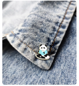 Detail view of a cartoon panda enamel pin worn on the collar of a blue denim jacket