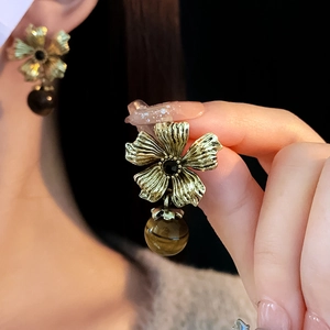 Détail de boucles d'oreilles fleur vintage en or avec perles d'œil de tigre et gemme noire