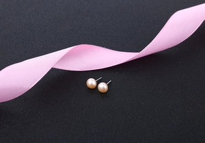 Macro shot of minimalist pink freshwater pearl stud earrings on a dark textured background