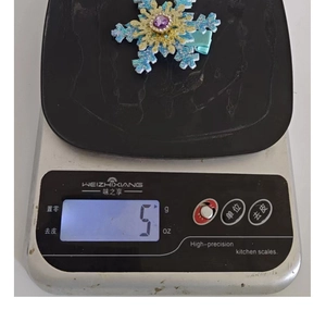 Detail showing a blue snowflake hair clip with rhinestones being weighed on a scale
